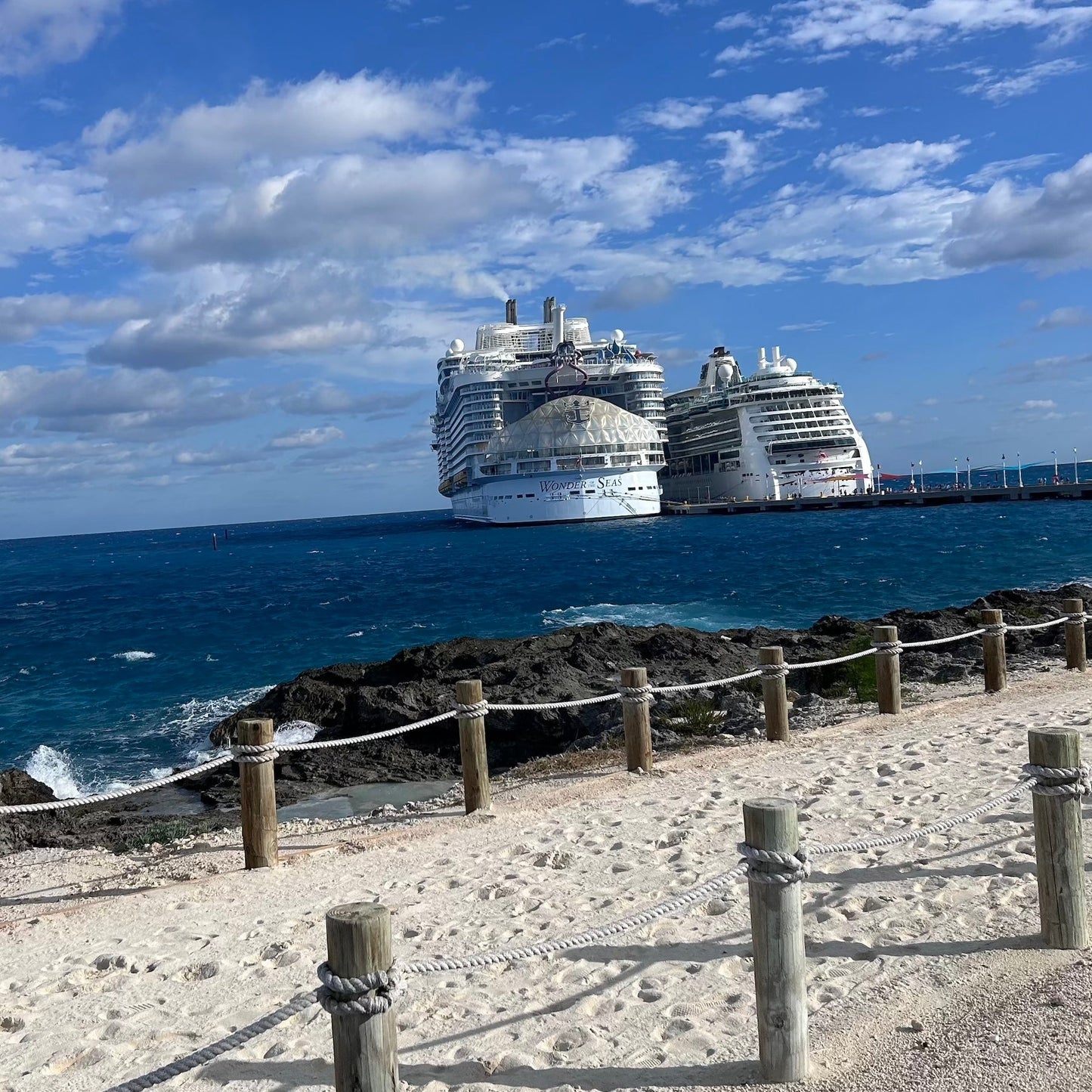 Two cruise ships docked at a pier with a clear blue sky and ocean.